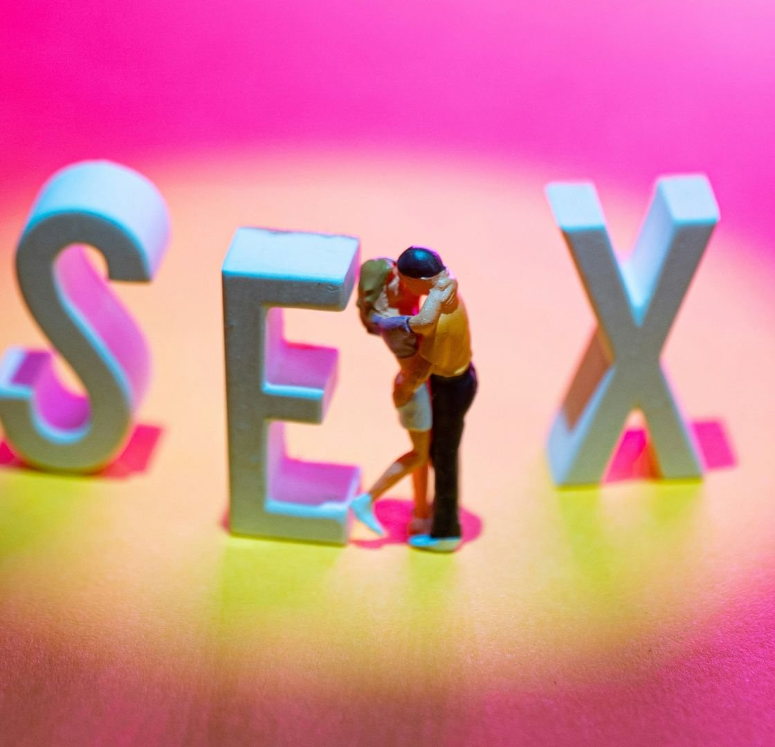 Miniature heterosexual couple embracing within the word "SEX". Sexual Health concept.